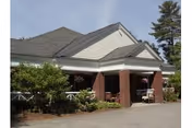 Covered front entrance with a porte-cochere supported by brick columns, white trim and surrounding shrubs under a pitched roof.