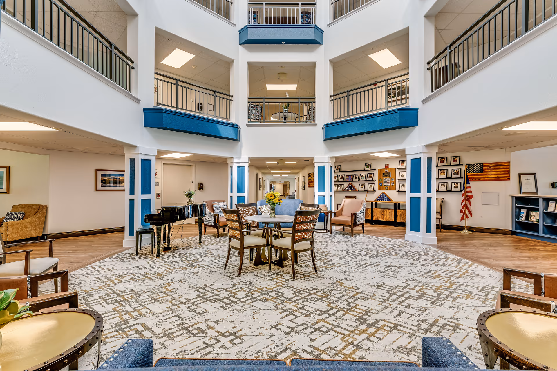 Open two-story atrium lounge with seating, a central table, a grand piano, and balconies overlooking the space.