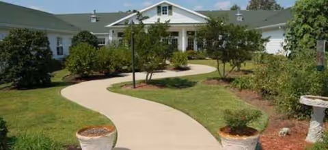 Curved walkway leads to a single-story Brookdale building with landscaped trees and shrubs.