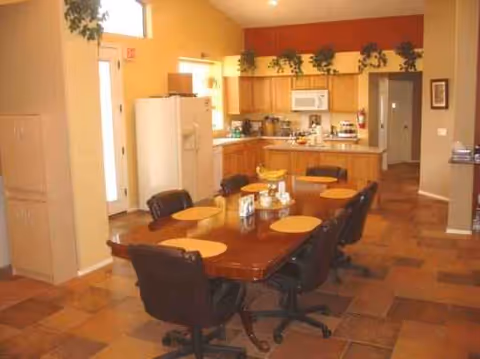 A dining area with a long wooden table and chairs in a warm kitchen.