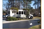 A white shuttle bus parked on a paved driveway surrounded by trees and bushes in a residential or facility area during daytime. The bus has the text 'Covenant Towers' on its side.
