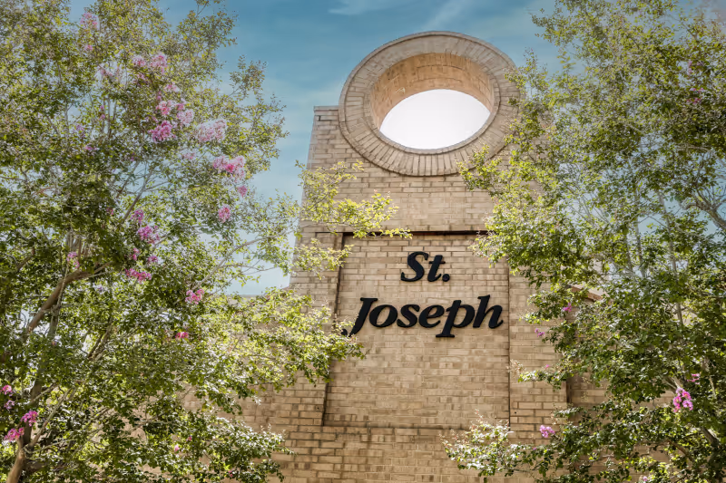 Brick front facade of the St. Joseph building with a circular architectural opening and surrounding trees with pink blossoms.