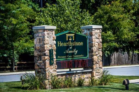 Stone entrance sign reads Amity Place, surrounded by green landscaping and trees.