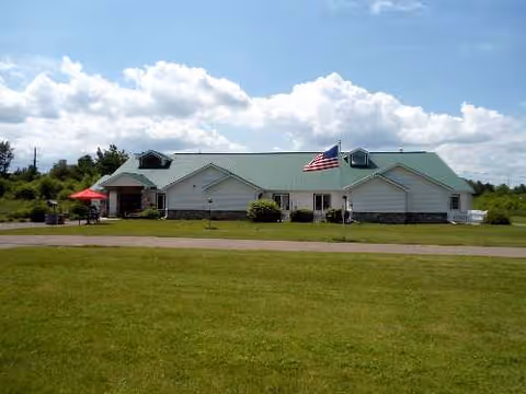 Single-story facility with green roof, American flag, and open lawn in front.
