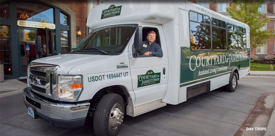 A Courtyard at Jamestown shuttle bus parked in front of the facility entrance with a driver leaning from the open window.