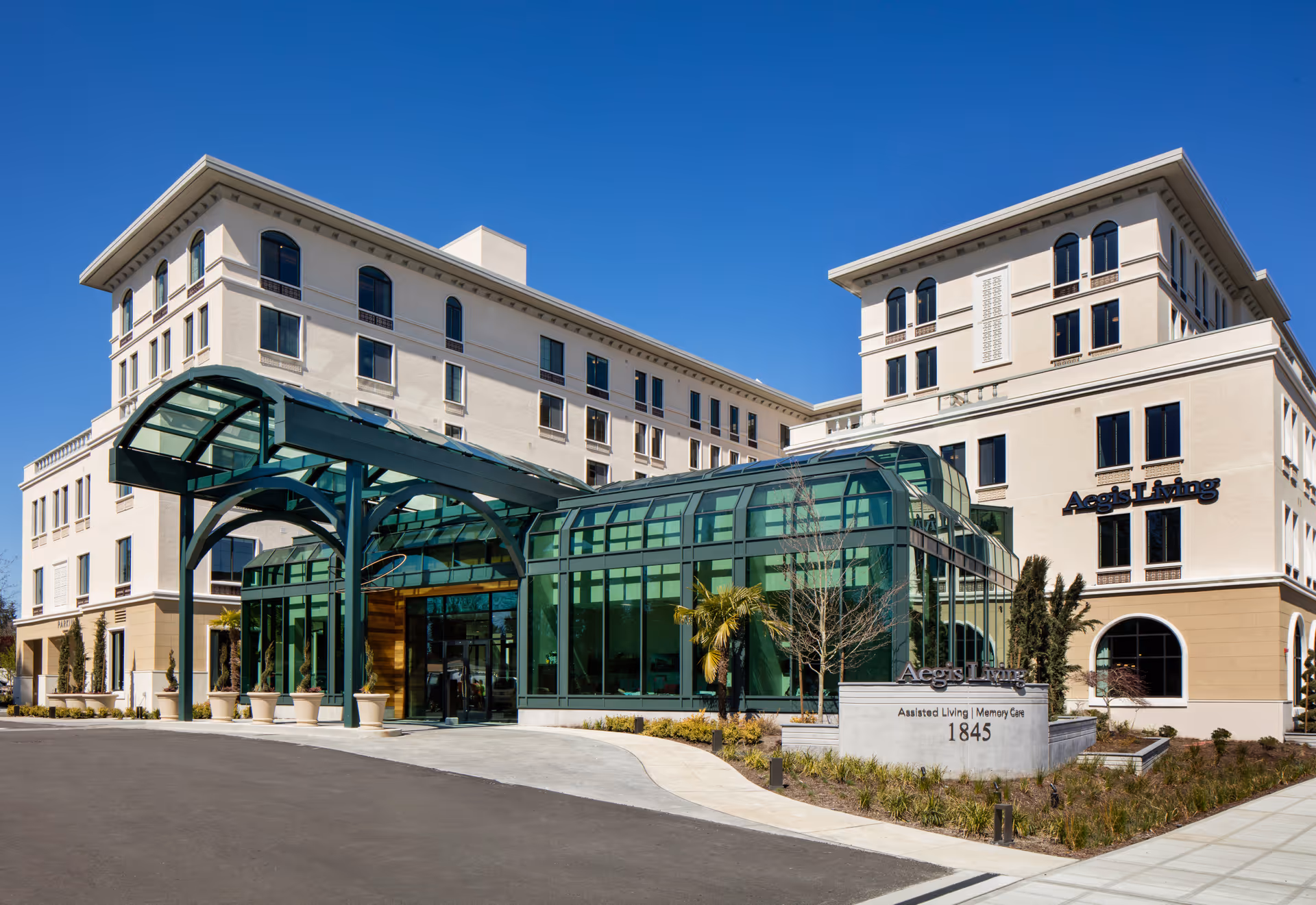 Front exterior of the Aegis Living Bellevue Overlake assisted living building with a glass entry canopy and landscaped driveway.
