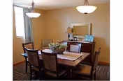 Dining room with a wooden table and six chairs, a sideboard with a mirror and lamps, and a window with curtains.