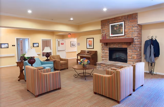 Common lounge with striped armchairs, sofas, a stone fireplace, piano, and coffee table.