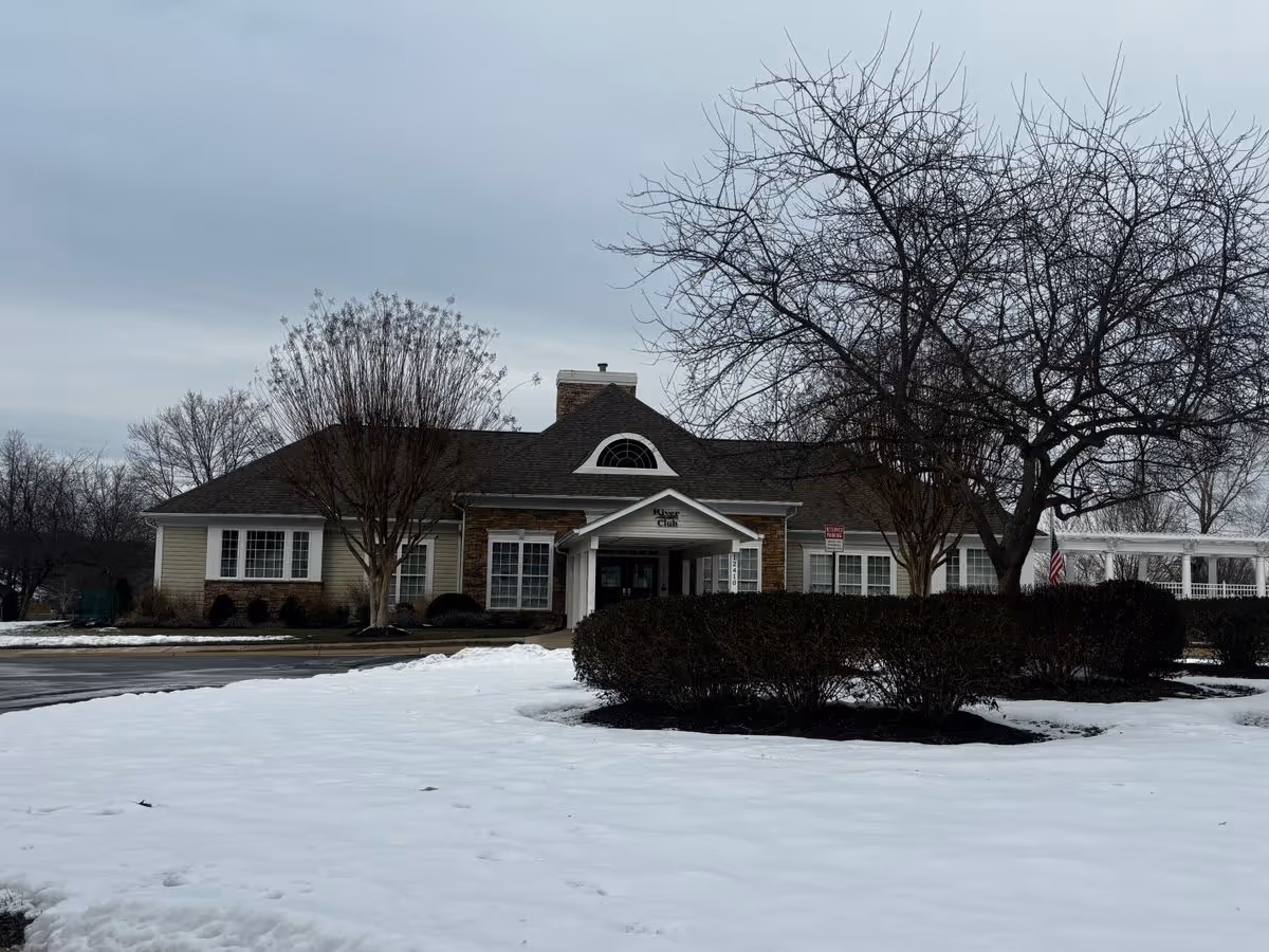 Front exterior of a single-story building with a covered entrance, snow-covered lawn, and bare trees.