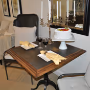 Small dining table set for two with a cake on a pedestal, two glasses of red wine, napkins, and a candelabra between two chairs in a cozy interior.