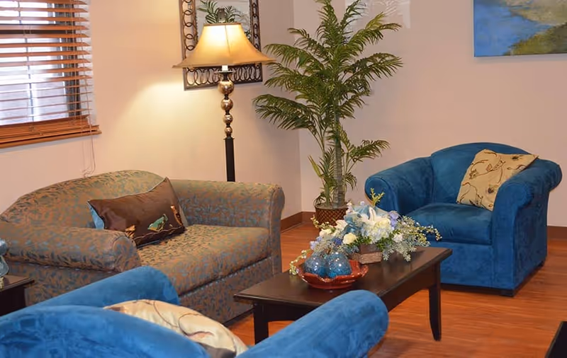 Cozy seating area with blue armchairs and a patterned sofa around a coffee table topped with flowers and decorative bowls.
