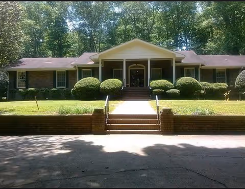 Front view of Heather House Personal Care facility with brick steps and trimmed bushes.