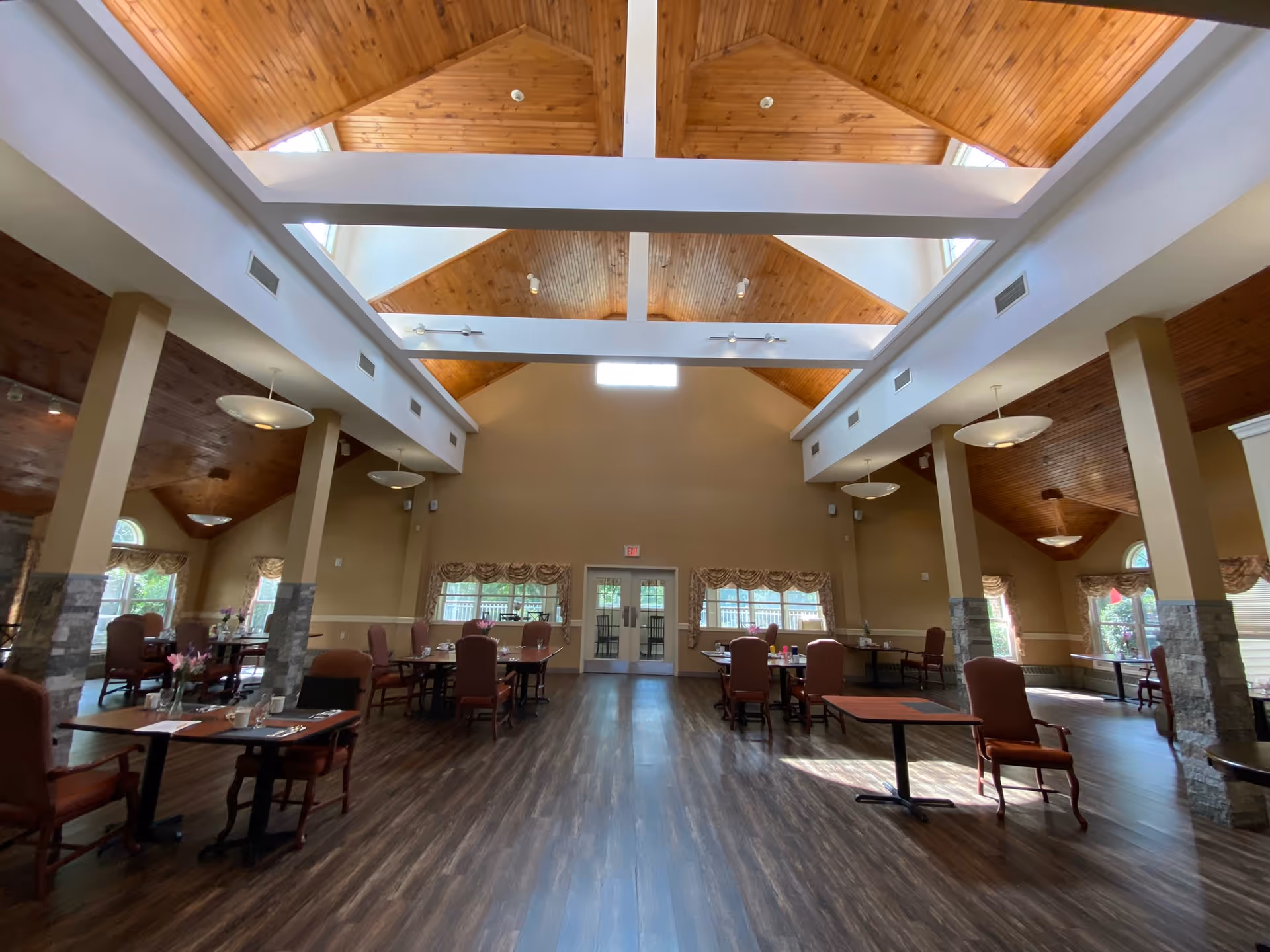 Spacious dining room with high vaulted wooden ceilings and tables and chairs arranged on a dark wood floor.