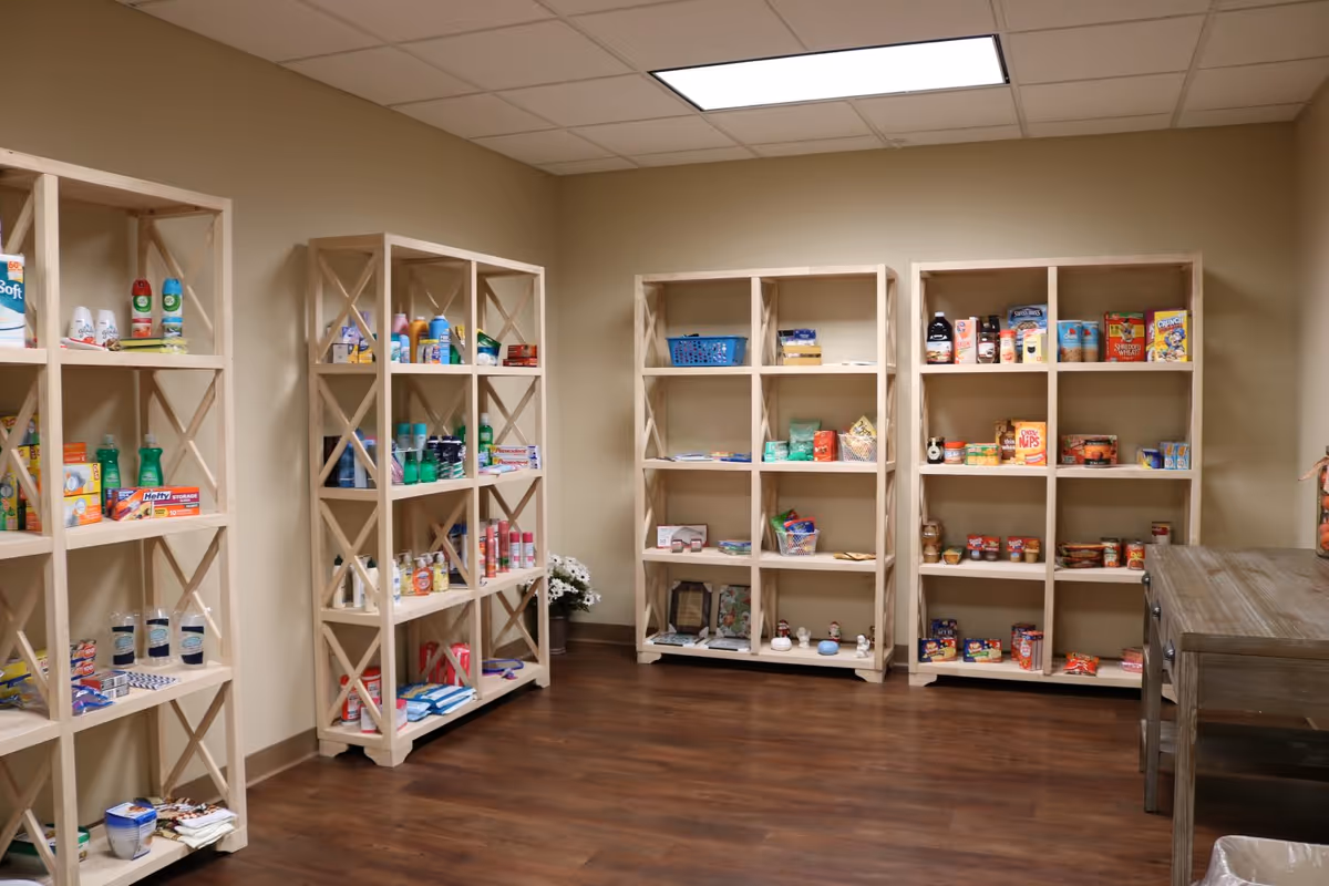 Wooden shelving units stocked with food, toiletries, and household items in a small interior room.