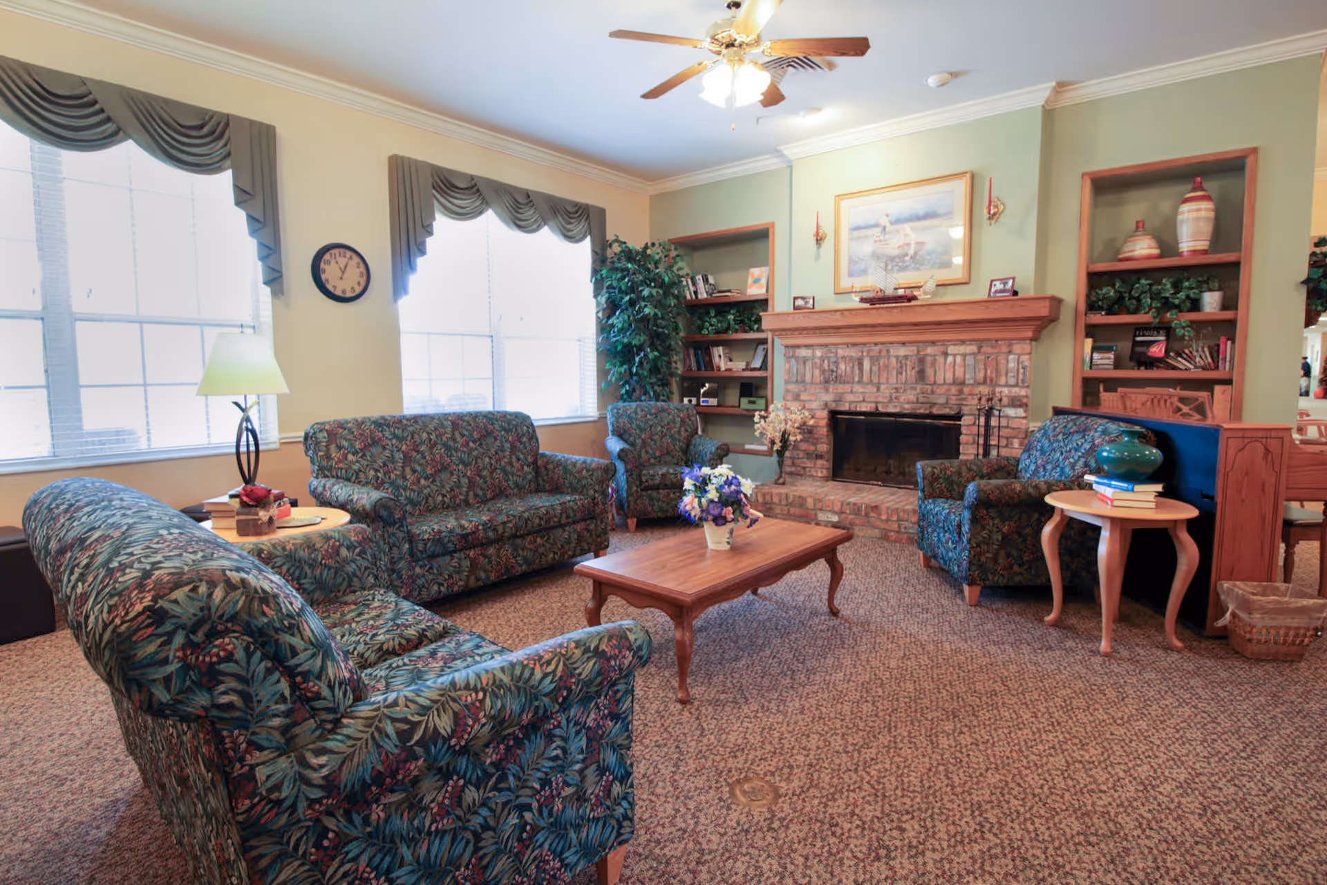 Cozy communal living room with patterned sofas and armchairs around a wooden coffee table facing a brick fireplace.
