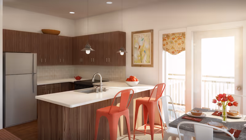 Modern kitchen with wooden cabinets, a stainless steel refrigerator, a white countertop island with a sink and two red bar stools. There are two pendant lights hanging above the island. A bowl of red apples is on the counter. To the right, there is a dining table set with plates, bowls, napkins, and a vase of red tulips. A door with a window and a floral curtain leads to an outdoor balcony.