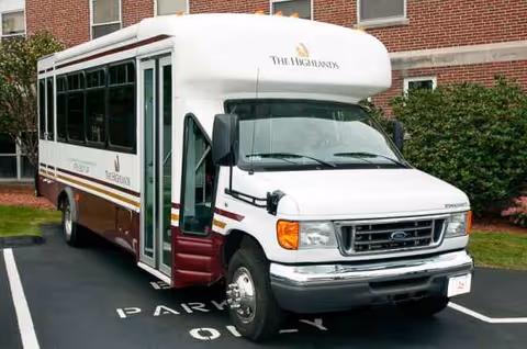 White Highlands shuttle bus parked in a lot beside a brick building.