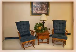 Two blue upholstered chairs flank a wooden side table with a lamp and plant.