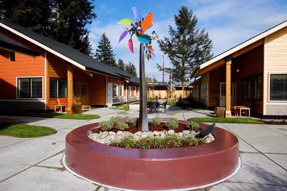 Central outdoor courtyard with a circular planter and colorful wind sculpture between single-story cottage buildings.