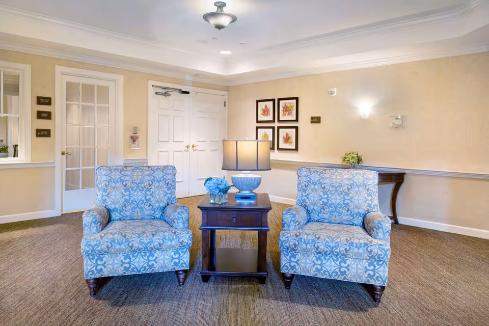 Two patterned armchairs flanking a wooden side table with a lamp in a well-lit seating area.