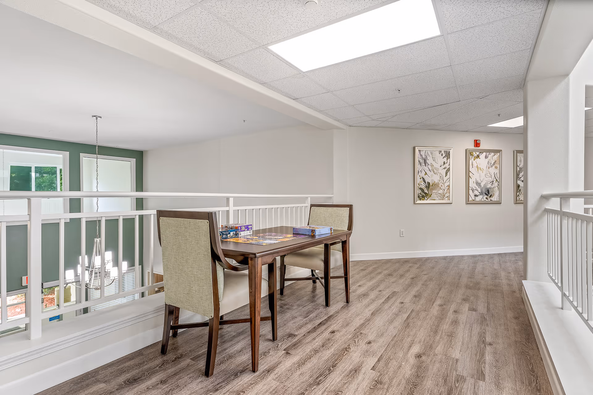 Bright upstairs common area with a small table and two chairs beside a white railing overlooking the foyer.