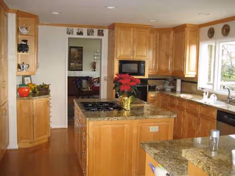 Bright kitchen with wooden cabinets, granite countertops, central island, and poinsettia centerpiece.