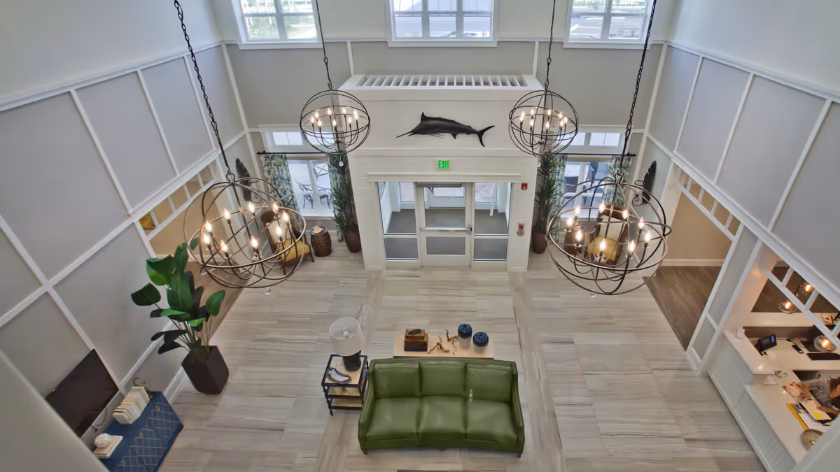 High-ceilinged lobby with large globe chandeliers, a green sofa, and double entry doors beneath a mounted fish sculpture.
