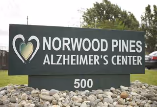 A large outdoor sign reads Norwood Pines Alzheimer's Center, set on a rock bed.