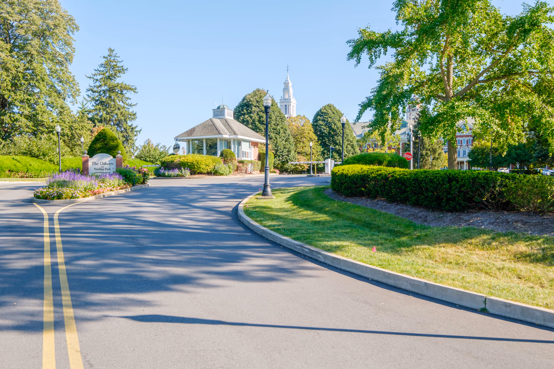 Curved driveway and landscaped entrance to The Osborn Senior Living with a small pavilion, lamp posts, and trees.