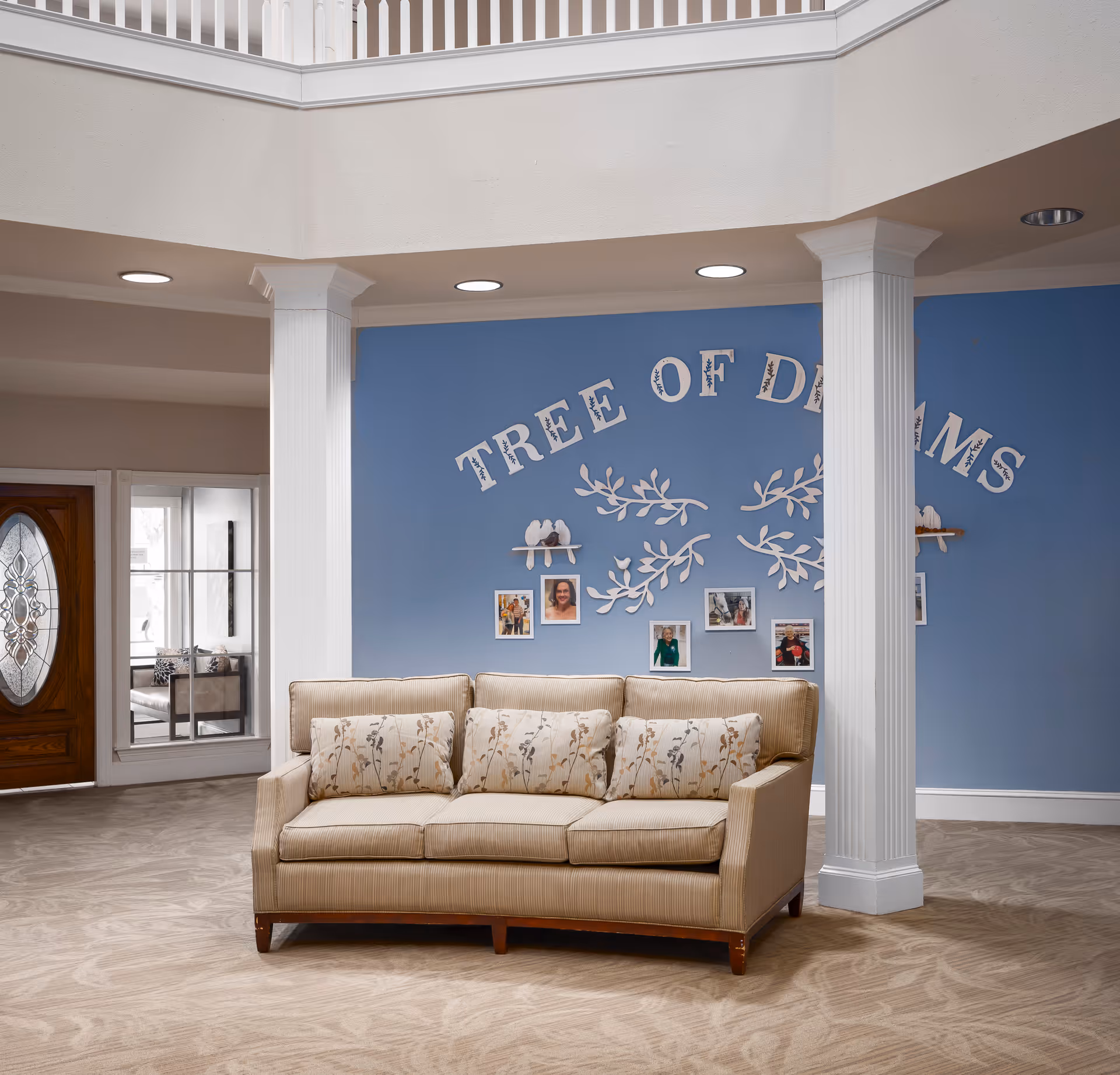 Lobby seating area with a beige sofa in front of a blue wall decorated with the words "Tree of Dreams", framed photos, and white columns.