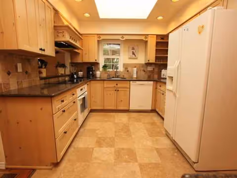 Bright L-shaped kitchen with wooden cabinets and appliances in a senior living facility.