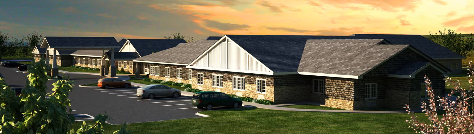 Exterior view of a single-story senior living facility building with a stone and shingle facade, multiple windows, and a parking lot with several cars parked. The scene is set during sunset with a partly cloudy sky and surrounding greenery.