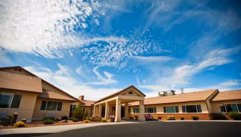 Exterior view of a single-story senior living facility with a covered entrance and blue sky