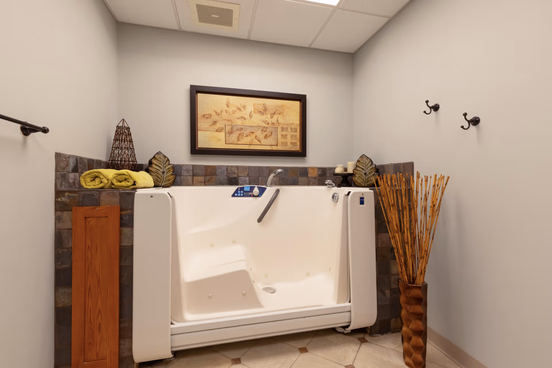 Accessible walk-in bathtub in a small spa-like bathroom with towels, wall art, and decorative bamboo accents.