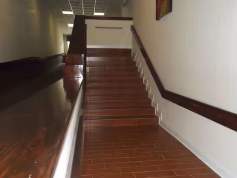 Indoor staircase with wood steps and dark handrails along a hallway in a residential facility.