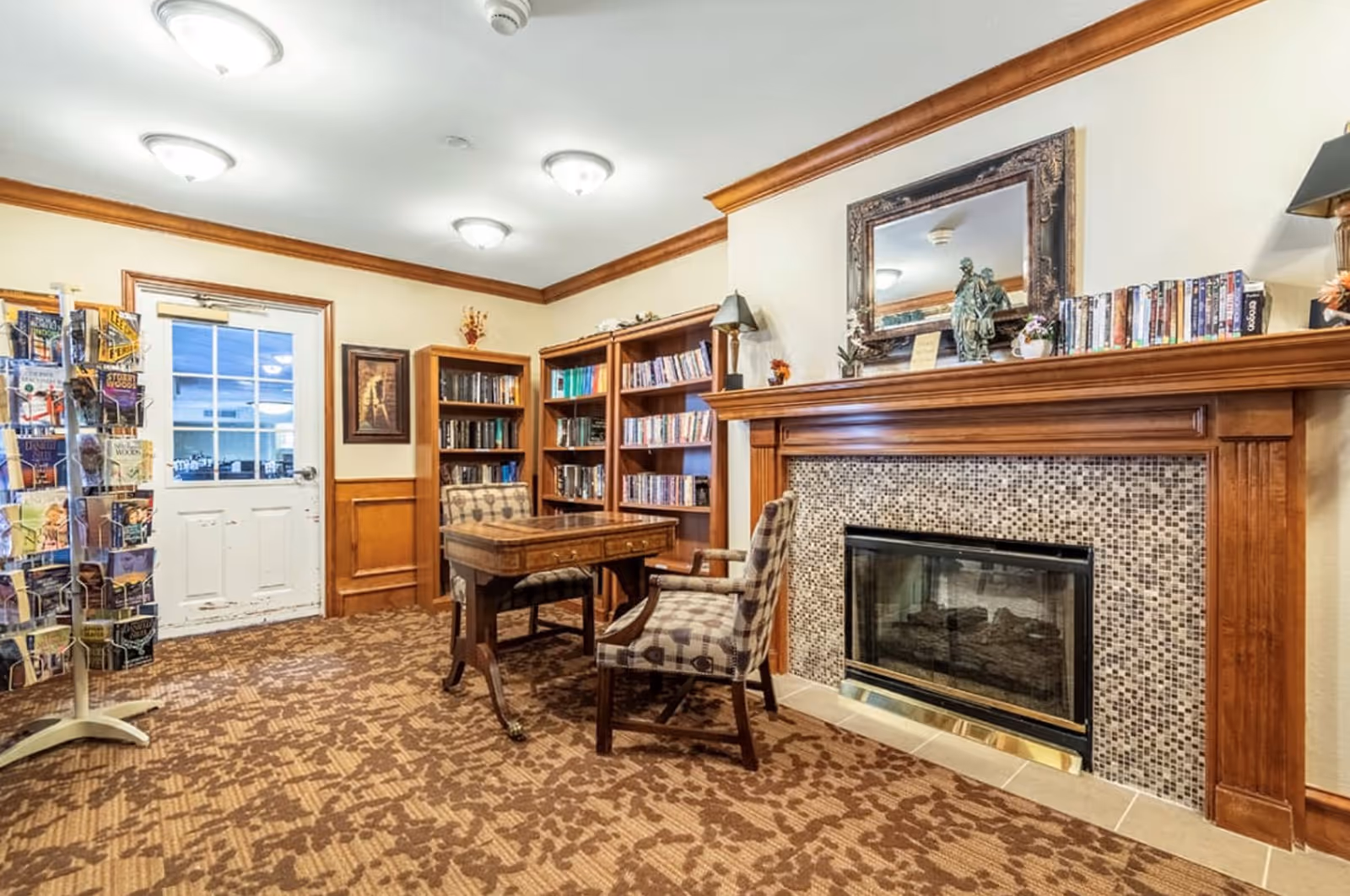 Cozy common room with a fireplace, bookshelves, a table and chairs, and a brochure rack.