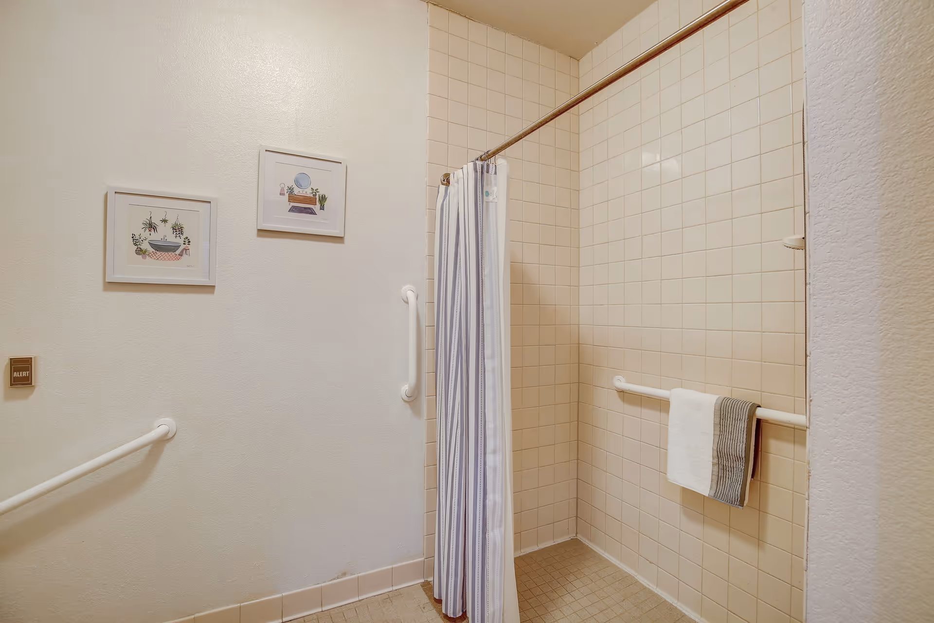 Accessible tiled walk-in shower with grab bars, a striped shower curtain, and a towel hanging on a rail.