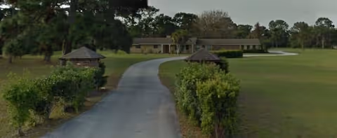 Long driveway curves toward a Pinewood Estates building amid green lawns and hedges.