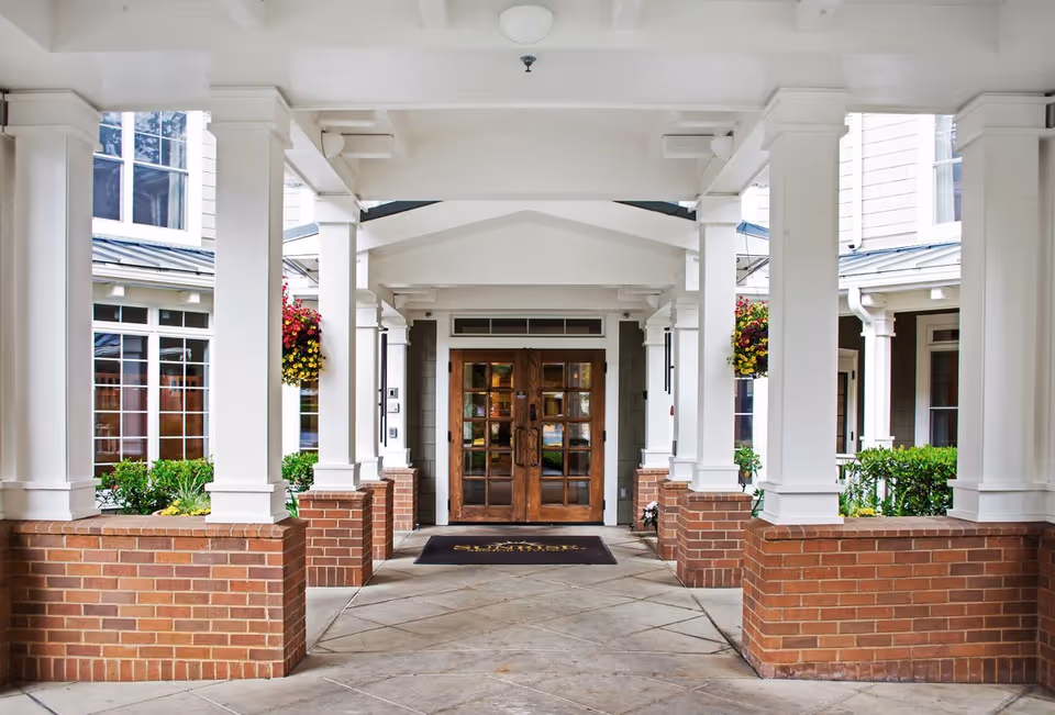 Covered entryway with white columns, brick planters, hanging flower baskets, and wooden double doors.