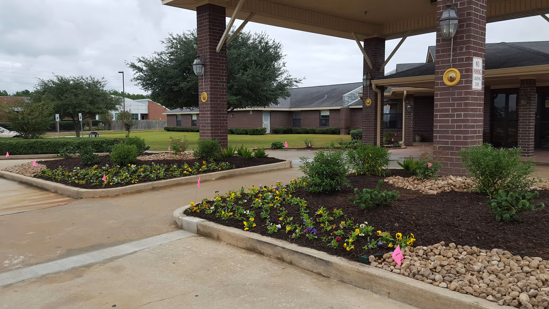 Exterior view of a brick-front entrance with a covered drop-off and landscaped flower beds.