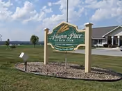 A green wooden sign reading "Arlington Place at Red Oak" stands on a landscaped lawn with the facility building visible in the background.