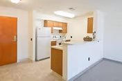 Compact kitchen area with white appliances, island counter, and cabinets in a senior living unit.