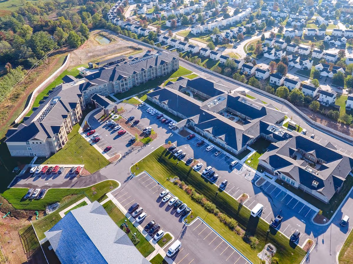 Aerial view of a senior living campus with multiple connected buildings, parking lots, and a surrounding residential neighborhood.