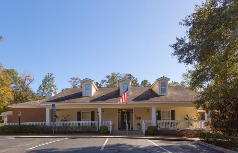 Single-story memory care building with a front porch, American flag, and parking spaces under a clear sky.
