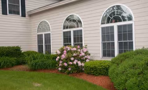 Beige building exterior with arched windows and manicured shrubs.