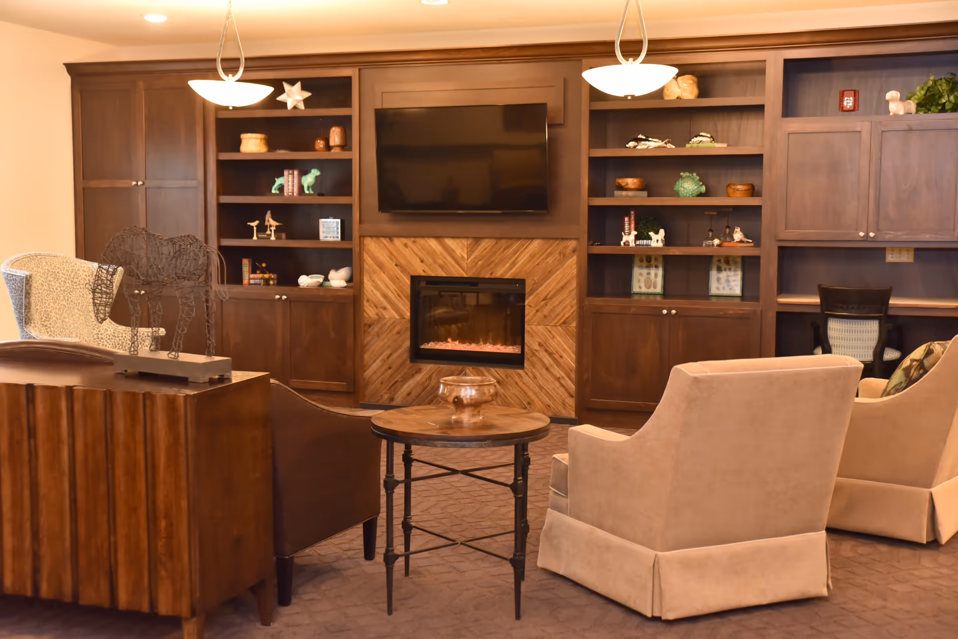 Cozy communal lounge with armchairs facing a wall-mounted TV and fireplace set within built-in wooden shelving.