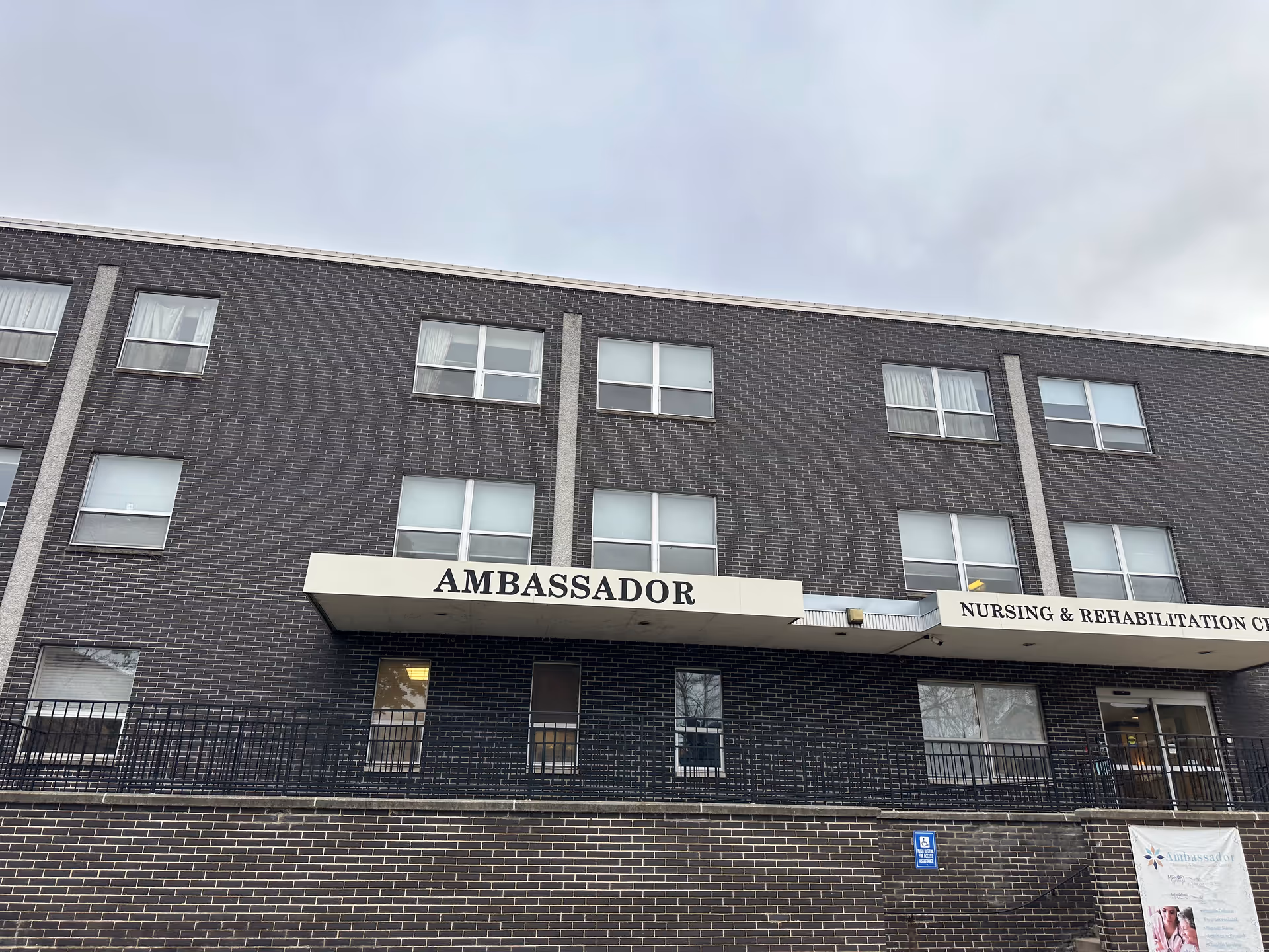 Front facade of a three-story brick building with an 'AMBASSADOR' sign and additional 'Nursing & Rehabilitation' signage.