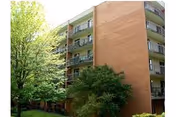 Brick multi-story apartment building with balconies surrounded by trees and grass.