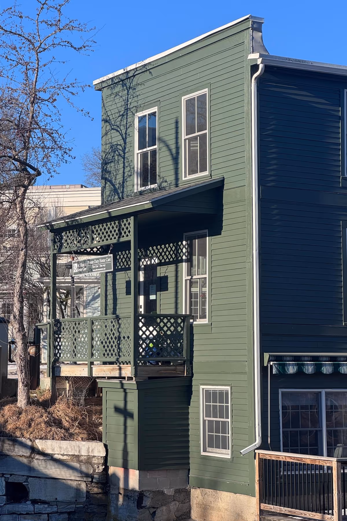 Green two-story building with a covered porch and balcony under a clear blue sky.