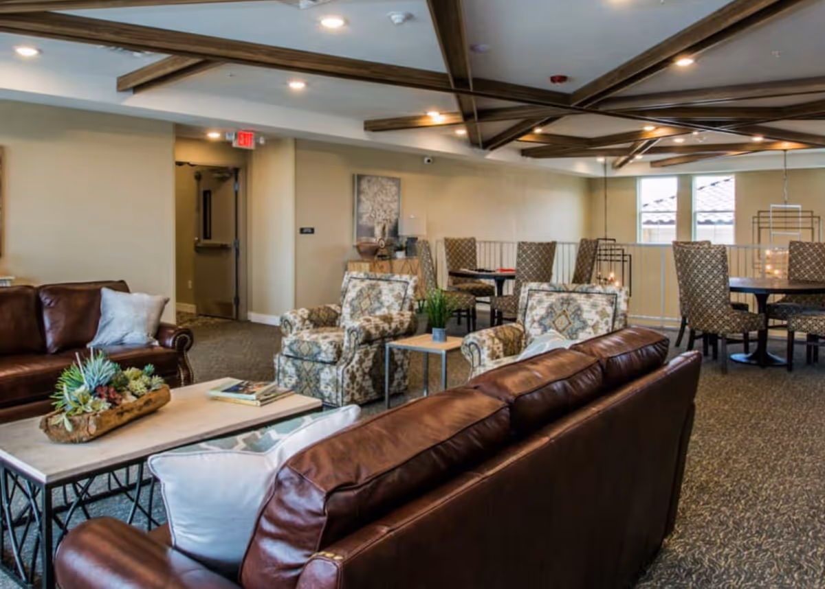 Communal lounge with leather sofas, patterned armchairs, coffee tables and dining tables under decorative ceiling beams.